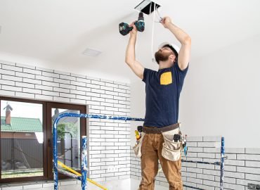 Electrician Builder at work, installation of lamps at height. Professional in overalls with a drill on the background of the repair site.